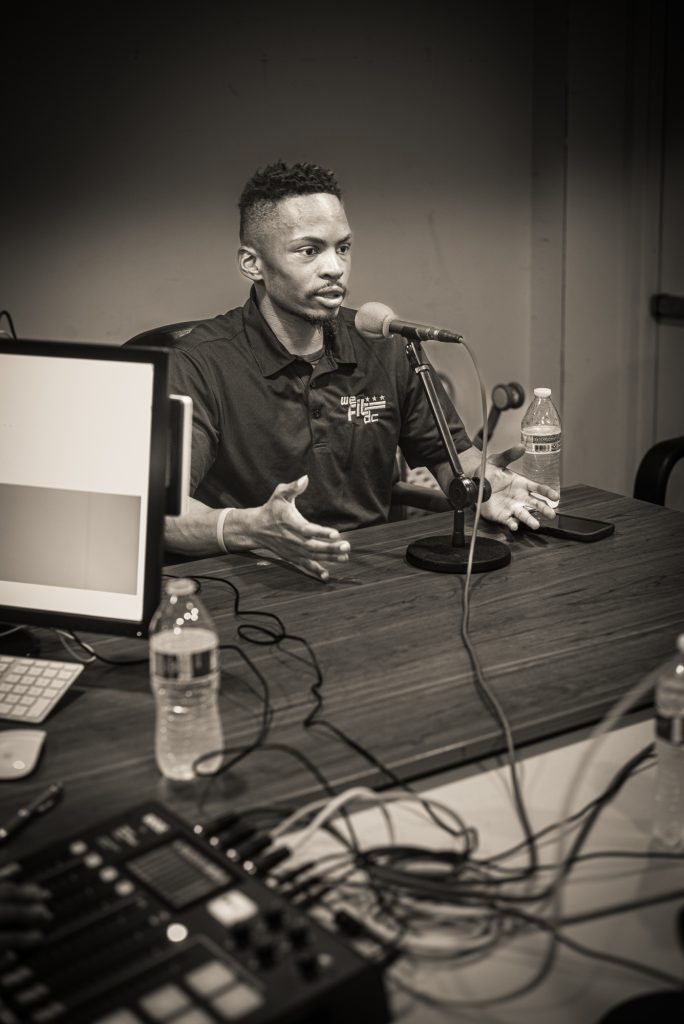 Joe Houston Jr. is a guest on an episode of the podcast Solutions from the Yard, September 2023. He's sitting at a table behind a microphone with his hands open.